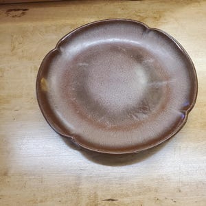 May include: A brown ceramic plate with a white glaze and a scalloped edge.