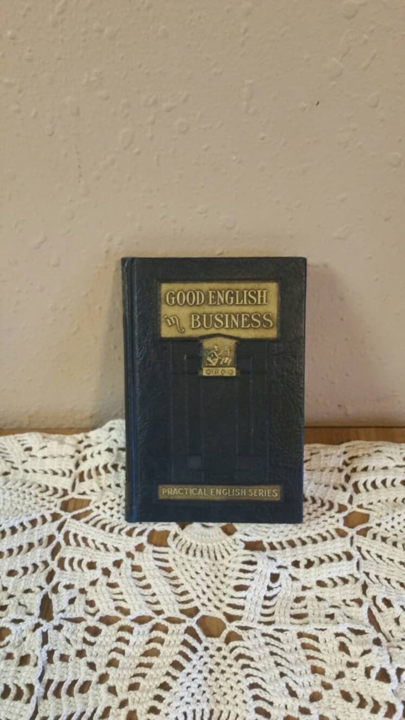 May include: A vintage blue book titled "Good English in Business" with gold lettering and a gold emblem. The book is part of the "Practical English Series".