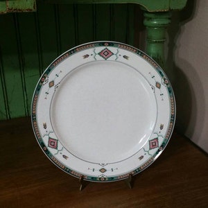 Może przedstawiać: Biały ceramiczny talerz obiadowy z zielonym, brązowym i różowym geometrycznym wzorem wokół krawędzi.