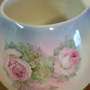 May include: A white ceramic jug with a blue and pink ombre glaze. The jug is decorated with a floral design of pink roses and green leaves.