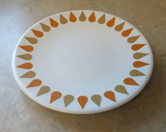 May include: A white ceramic plate with a brown and orange teardrop design around the edge.