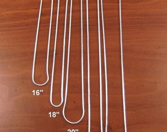 May include: Five silver chains of different lengths, laid out on a wooden surface. The chains are labeled with their lengths in inches: 16", 18", 20", 22", and 24".