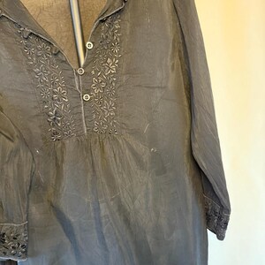 May include: Black long-sleeve blouse with floral embroidery around the neckline and cuffs. The blouse has a button-down front and a mandarin collar. The fabric appears to be lightweight and slightly textured.