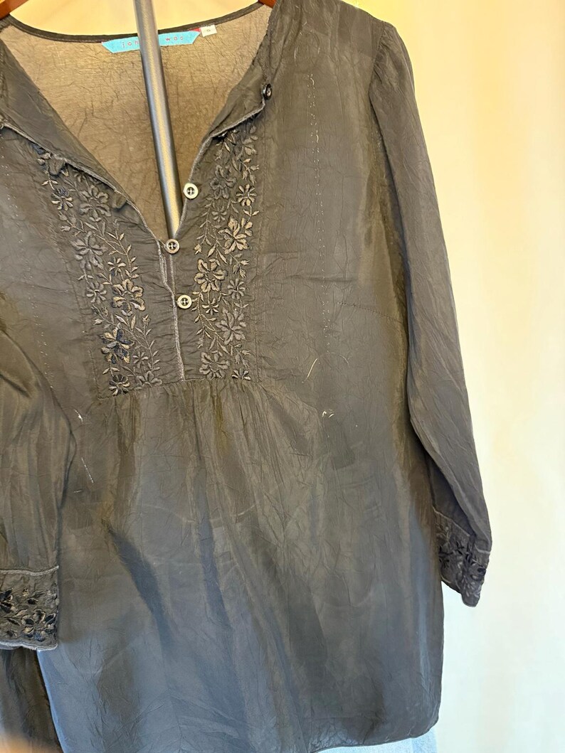 May include: Black long-sleeve blouse with floral embroidery around the neckline and cuffs. The blouse has a button-down front and a mandarin collar. The fabric appears to be lightweight and slightly textured.
