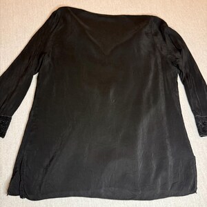 May include: Black long-sleeve tunic with a V-neck and a slightly textured appearance. The sleeves have decorative embroidery at the cuffs. The tunic is made of a lightweight fabric and has a loose, flowing fit.