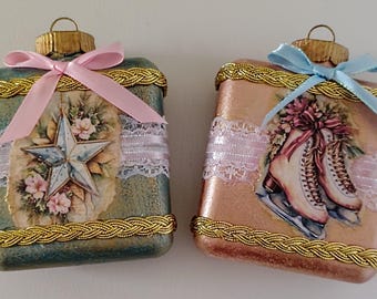 May include: Two decorative Christmas ornaments. One is teal with a star and floral design, the other is peach with ice skates. Both have gold trim, pink or blue bows, and lace accents.