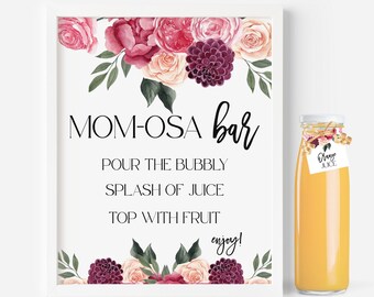 May include: A white sign with pink and burgundy floral illustrations and the text "MOM-OSA bar POUR THE BUBBLY SPLASH OF JUICE TOP WITH FRUIT enjoy!" A bottle of orange juice with a tag that says "Orange Juice" is to the right of the sign.