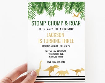 May include: A rectangular party invitation card featuring green watercolor palm leaves at the top and gold dinosaur silhouettes at the bottom. The text reads STOMP, CHOMP & ROAR, LET'S PARTY LIKE A DINOSAUR, JACKSON IS TURNING THREE, and event details.