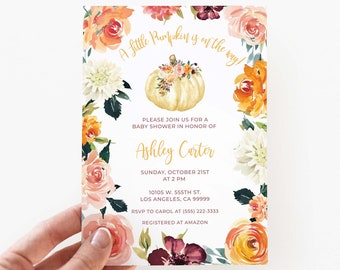 May include: A baby shower invitation with a watercolour design. The invitation features a pumpkin illustration surrounded by floral accents in shades of orange, pink, and white. Text includes the event details and the name Ashley Carter.