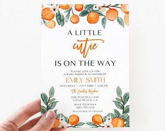 May include: A rectangular baby shower invitation card featuring watercolor orange illustrations with green leaves and white flowers at the top and bottom. The text reads A LITTLE cutie IS ON THE WAY, honoring Emily Smith on July 23rd at 2:30 PM.