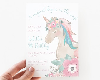 May include: A rectangular birthday invitation card featuring a watercolor illustration of a unicorn with a floral crown, pink and teal mane, and a horn. The text reads A magical day is on the way, Isabella's 5th Birthday, and event details.