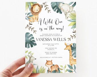 Może przedstawiać: Prostokątne zaproszenie na baby shower z akwarelowymi ilustracjami lwa, słonia, żyrafy i tygrysa w otoczeniu zielonych liści tropikalnych. Tekst brzmi A Wild One is on the way! Please join us for a baby shower in honor of Vanessa Wells, Saturday July 27th at 2 PM, 1234 Safari Rd, Miami, FL, RSVP to Jenna (305) 555-1212, Registered at Pottery Barn.