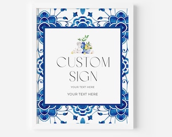 Op de afbeelding: Een ingelijst aangepast bord met een witte achtergrond en een blauwe bloemenrand. Het bord bevat de zwarte woorden "CUSTOM SIGN", met ruimte voor gepersonaliseerde tekst eronder. Bovenop staat een aquarel illustratie van een vaas met bloemen en citroenen.