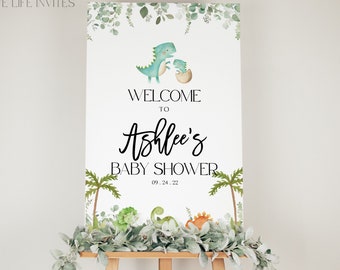 Könnte beinhalten: Ein Willkommensschild für eine Babyparty mit Illustrationen von Dinosauriern und Blättern. Auf dem Schild steht "Willkommen zu Ashlees Babyparty" mit dem Datum 09.24.22. Das Schild wird auf einer Holzstaffelei präsentiert.
