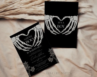 May include: Two black rectangular baby shower invitation cards featuring white skeleton hands forming a heart shape. One card displays the text A LITTLE BOO IS ALMOST DUE and the other IT'S A BOY. Both cards include floral illustrations at the bottom.