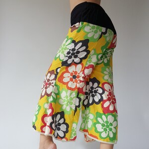 May include: Wide-leg pants with a floral print in shades of yellow, green, red, black, and white. The pants have a white lace trim around the bottom hem.