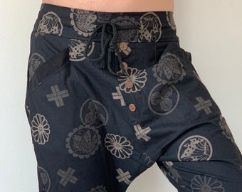 May include: Black trousers with a drawstring waist and a pattern of stylised flowers and fish. The trousers are cropped and have a loose fit.