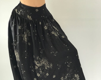May include: Black harem pants with a floral print. The pants have a wide leg and a gathered waist.