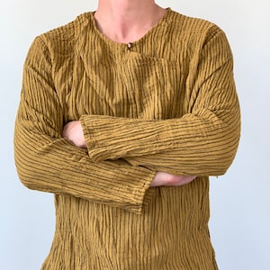 May include: A long-sleeved shirt with a striped pattern in shades of brown and black. The shirt has a round neckline and a button closure at the neck.