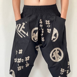 May include: Black pants with an elastic waistband and side pockets. The pants have a unique design featuring beige Japanese characters and floral patterns.