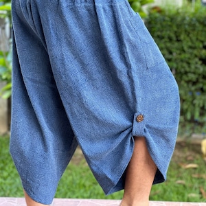 May include: Blue cropped pants with an elastic waistband and a button detail at the hem. The pants have a relaxed fit and a textured appearance, suitable for casual wear. The fabric appears to be a lightweight material.