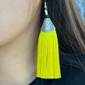 May include: A pair of yellow tassel earrings with a silver and black metal top.