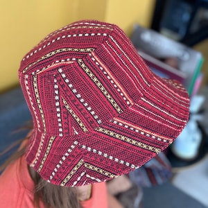 以下が含まれることがあります： 黒、白、黄色の幾何学模様が施された赤いバケットハット