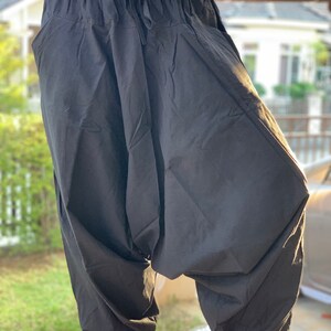 May include: Black cotton pants with a drawstring waist and a loose, baggy fit. The pants have a wide leg and a gathered ankle.