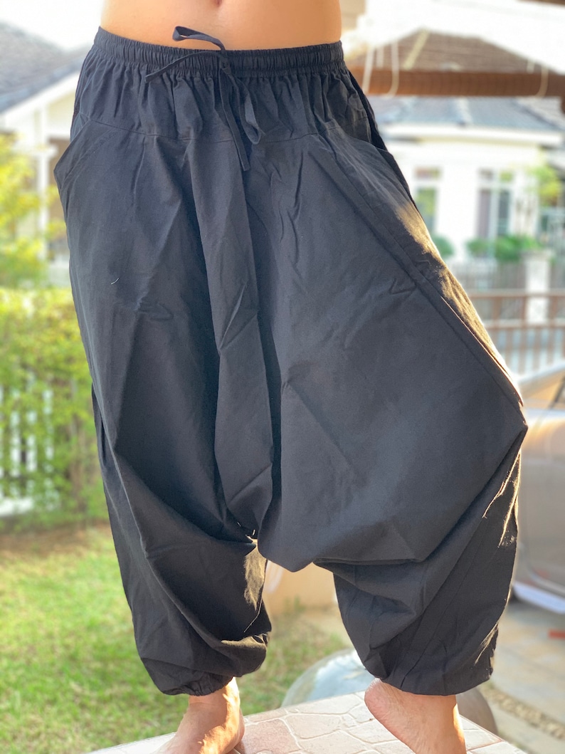 May include: Black cotton pants with a drawstring waist and a loose, baggy fit. The pants have a wide leg and a gathered ankle.