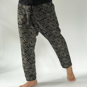 May include: Black and beige patterned pants with a black waistband. The pants have a loose fit and are made of a lightweight fabric.