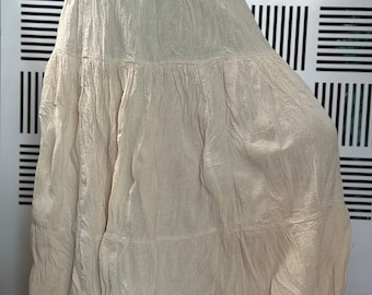 May include: A long, tiered skirt in a light beige color. The skirt is made of a soft, flowing fabric and has a relaxed fit.