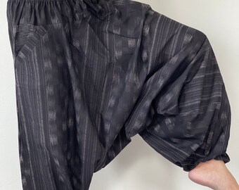May include: Black harem pants with a vertical striped pattern in gray and white. The pants have a drawstring waist, pockets, and gathered ankles. The fabric appears lightweight and comfortable.