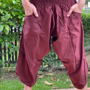 May include: Burgundy-colored harem pants with an elastic waistband and pockets. The loose-fitting pants are cropped at the calf and have a relaxed, comfortable style. The pants are made of a lightweight fabric, perfect for warm weather.