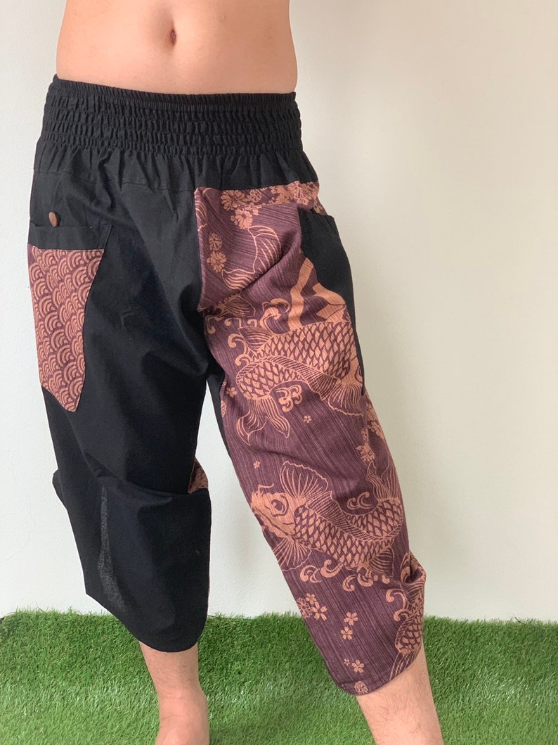 May include: Black cropped pants with a brown and gold patterned design featuring koi fish and floral motifs. The pants have an elastic waistband and a drawstring.