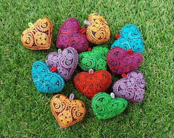 May include: A collection of 11 colourful heart-shaped ornaments with intricate embroidered designs. The hearts are made of fabric and have a variety of colours, including red, green, blue, purple, and orange.