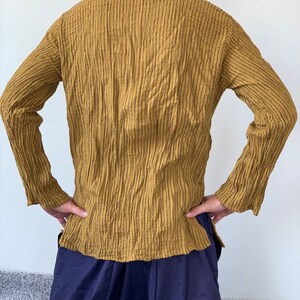 May include: A long-sleeved shirt in a mustard yellow colour with a textured, ribbed fabric. The shirt has a v-neck and a relaxed fit.