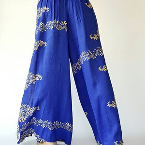May include: Wide-leg trousers in a vibrant blue colour with a gold floral pattern. The trousers have an elastic waistband and a flowing silhouette.
