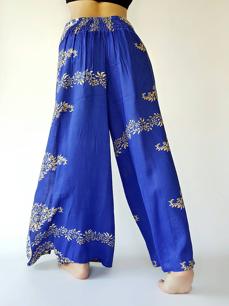 May include: Wide-leg trousers in a vibrant blue colour with a gold floral pattern. The trousers have an elastic waistband and a flowing silhouette.