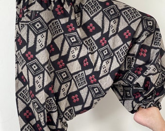 May include: Black and beige patterned pants with a red diamond design. The pants have an elastic waistband and a loose, flowing fit.