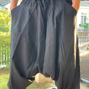 May include: Black cotton pants with a drawstring waist and side pockets. The pants are loose fitting and have a baggy style.
