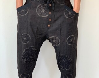 May include: Black cropped trousers with a drawstring waist and button fly. The trousers feature a unique design with circular patterns and Chinese characters.