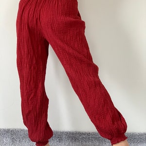 May include: Red cotton pants with a loose, flowing fit and elastic waistband. The pants have a textured, crinkled appearance.