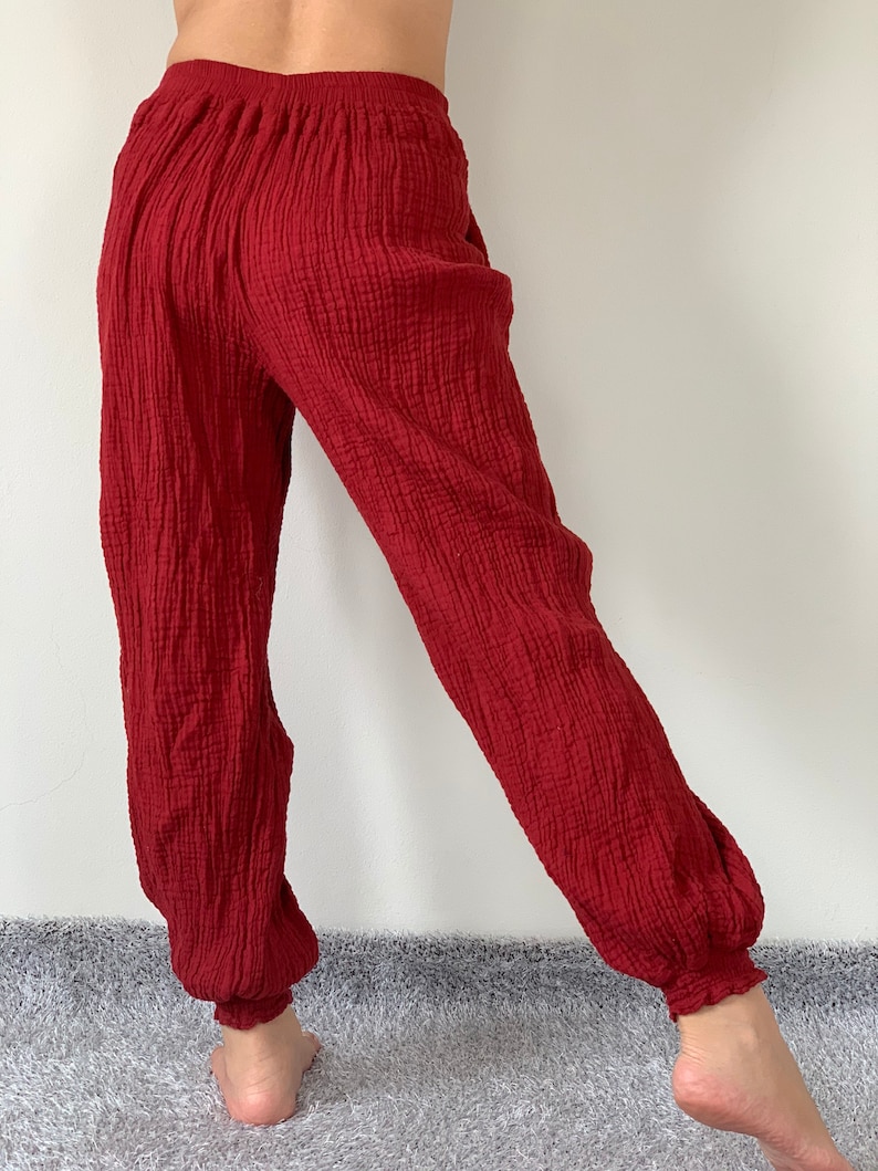 May include: Red cotton pants with a loose, flowing fit and elastic waistband. The pants have a textured, crinkled appearance.
