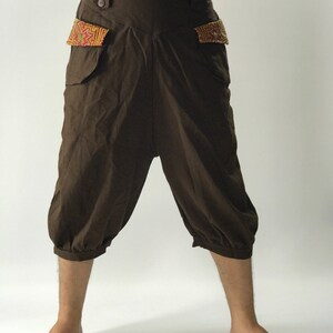 May include: Brown linen pants with a wide leg and a gathered hem. The pants have a button closure and two pockets with colorful embroidered details.