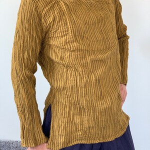 May include: A long-sleeved shirt with vertical stripes in a mustard yellow colour. The shirt has a round neckline and a single button fastening at the neck.