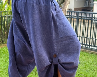 Puede incluir: Un pantalón corto de color azul oscuro con corte holgado, cintura elástica con cordón, un bolsillo lateral de parche y una trabilla decorativa en la parte inferior de la pierna asegurada con un botón marrón, hasta media pantorrilla.
