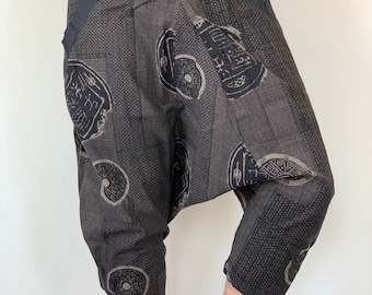 May include: Black and grey patterned trousers with a drawstring waist. The trousers have a loose, baggy fit and feature a unique design with circular patterns.
