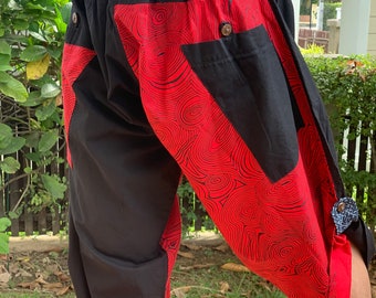 May include: Black and red patterned shorts with an elastic waistband. The shorts feature a unique design with red fabric panels adorned with a black swirl pattern. The shorts have a button closure and a relaxed fit.