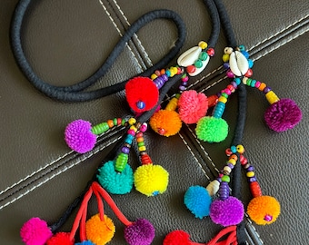 May include: A black cord necklace with colorful pom-poms and beaded accents. The necklace features red, orange, yellow, green, blue, and purple pom-poms. The necklace also has white seashells.