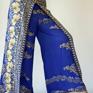 May include: Wide-leg trousers in blue with a gold and white floral print. The trousers have a wrap-around style and a high waist.